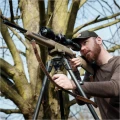 Trójnóg Primos Trigger Stick Apex - zdjęcie w plenerze, myśliwy celujący z karabinu opartego na trójnogu, wśród drzew
