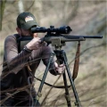 Trójnóg Primos Trigger Stick Apex - zdjęcie w plenerze, myśliwy celujący z karabinu opartego na trójnogu, wśród zarośli