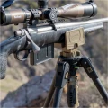 Trójnóg Primos Trigger Stick Apex - zbliżenie na karabin oparty na głowicy trójnogu z logo Primos, w tle skalisty teren
