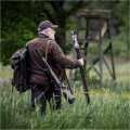Trójnóg Primos Trigger Stick Gen III™ 24-62'' - zdjęcie w plenerze, myśliwy idący przez łąkę w stronę ambony, z trójnogiem jako laską