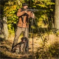 Trójnóg Primos Trigger Stick Gen III™ 24-62'' - zdjęcie w lesie, myśliwy z psem celujący z karabinu opartego na trójnogu