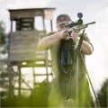 Trójnóg Primos Trigger Stick Gen III™ 24-62'' - zdjęcie w plenerze, myśliwy celujący z karabinu opartego na trójnogu, w tle ambona