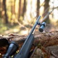 Strzelecka kamera sportowa na broń HIKMICRO HIKCam A7E karabin z zamontowaną kamerą oparty o pień drzewa podczas polowania w lesie.