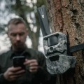 Dwupak kamera fotopułapka HIKMICRO T16 4G LTE - widok zamontowanej kamery na drzewie, mężczyzna z telefonem w tle